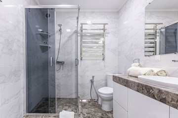 Interior of a modern bathroom with shower, in a small apartment, with white marble tiles