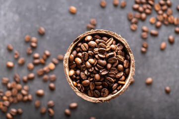 Obraz premium black coffee beans arabica, aromatic in a coconut dish, sprinkled beans on the table, close-up, top view