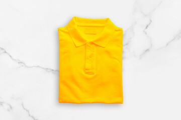 Yellow polo t-shirt on white marble floor background.