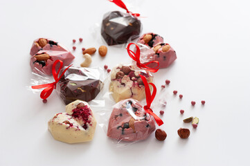 chocolates mix, in the form of hearts with pink, milk and white chocolate with strawberries, blueberries and almonds, tied with a ribbon, handmade, top view, on a white background
