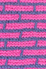 striped background of tunisian crochet fabric in basic stitch in pink with blue grid pattern