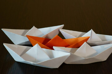 Several paper boats on the table. One of them is orange.