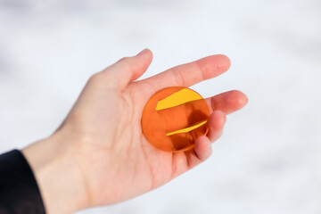 Small colored round transparent glass of golden yellow color in the hand of a man against a background of snow. Find concept
