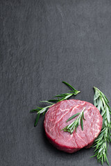 Fresh raw beef steak with rosemary stick on black stone background