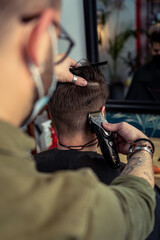 tatooed barber at work using a hair clipper on the neck of his customer