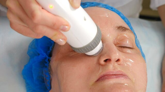 Facial lifting, wrinkle smoothing and rhytide effacement procedure. Hardware cosmetology treatment. Beautician moves manipulator with light on female face. Non-surgical face skin lifting in beauty