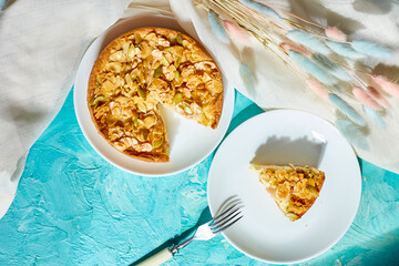 Piece of apple or pear pie, tart with caramel nuts on blue table with sunlight