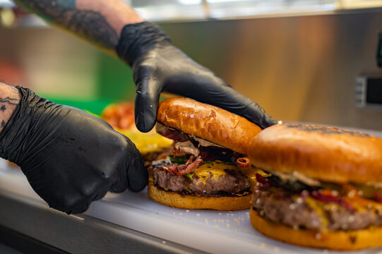 Tasty Close Up Shot of a Cook Preparing Burgers. Food Chef is Adding Souce on top of Buns with Sesame Seeds.