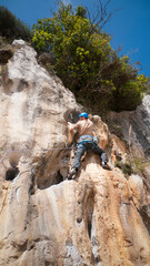 Joven barbudo con casco azul escalando en pared rocosa con cuerdas