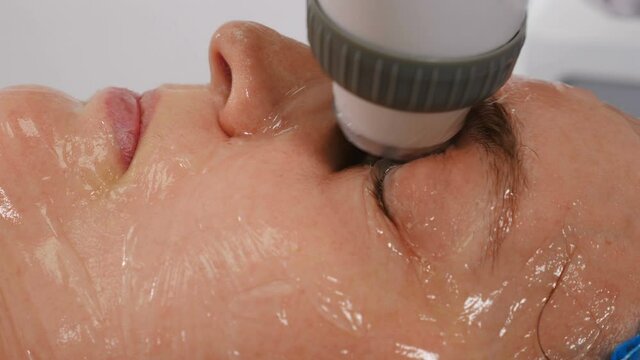 Facial lifting, wrinkle smoothing and rhytide effacement procedure. Hardware cosmetology treatment. Beautician moves manipulator with light on female face. Non-surgical face skin lifting in beauty
