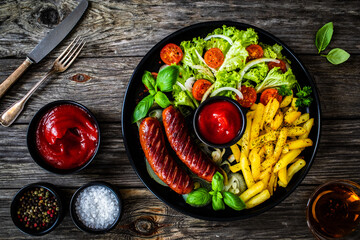 Fried sausages, French fries, onion and fresh vegetables on black table