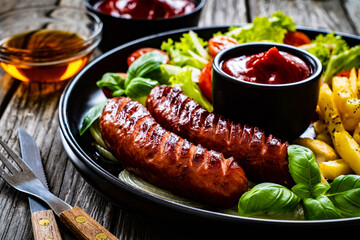Fried sausages, French fries, onion and fresh vegetables on black table