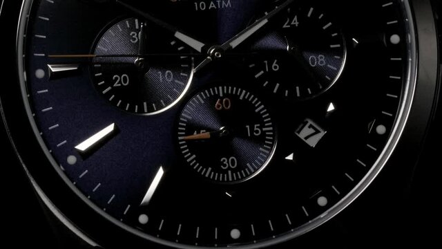 Swiss watch with dark blue clockface rotating with dramatically passing light while second arrows are running