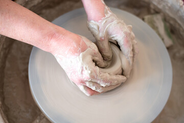 Woman working on potter's wheel. Hands sculpt cup from white clay pot. Workshop on modeling do plate. Potter works on potter's wheel. Concept:handmade, workshop, artist.