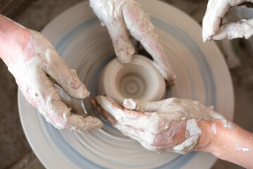 Women working on the potter's wheel. Hands of teacher show to student how to hold and push clay. Girl sculpt cup from white clay pot. Workshop on modeling do plate. Concept: handmade, workshop, artist