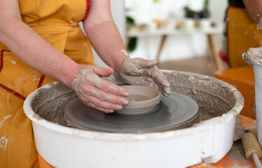 Woman working on potter's wheel, makes cup. Hands sculpt cup from white clay pot. Workshop on modeling do plate.  Concept:handmade, workshop, artist. Close-up