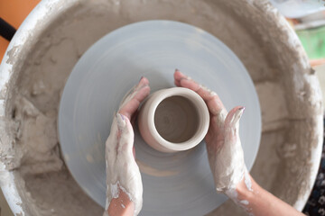 Fototapeta na wymiar Woman working on potter's wheel, makes vase. Hands sculpt cup from white clay pot. Workshop on modeling do plate. Concept: handmade, workshop, artist. Top view.