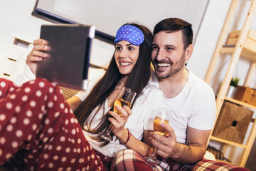 Smiling relaxed young couple using digital tablet in bed at home