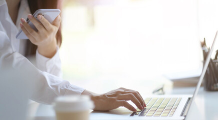 Cropped image of female holding smartphone getting message with confirmation making transaction on laptop computer,woman using mobile phone app for synchronizing data with netbook via bluetooth.