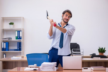 Young male furious employee holding hatchet in the office