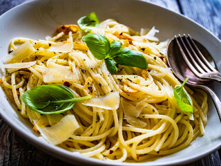 Spaghetti aglio e olio with parmesan and basil on wooden table
