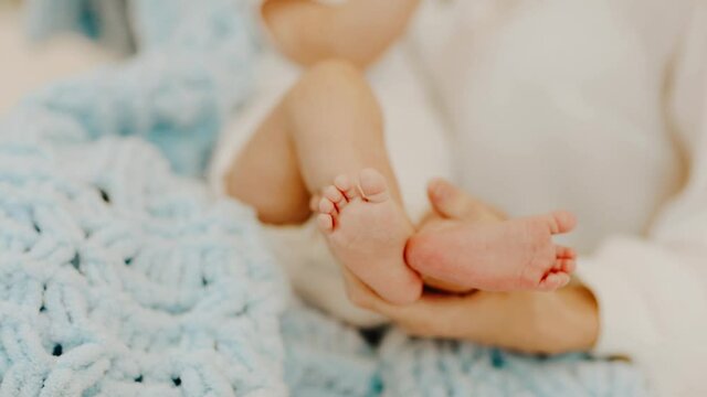 Mother's hands holding newborn's feet near soft blue blanket. Copy space.