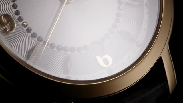 Luxury golden swiss made women watch with diamonds and ribbed pattern rotating while second arrow running by numbers and date. Closeup on black background