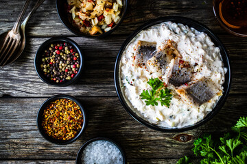 Marinated herring fillets in cream with pickled cucumber, parsley, onion and apple on wooden table 