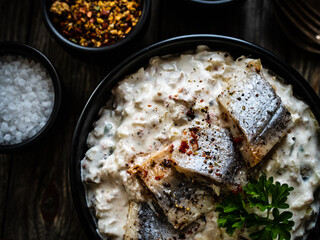 Marinated herring fillets in cream with pickled cucumber, parsley, onion and apple on wooden table 