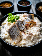Marinated herring fillets in cream with pickled cucumber, parsley, onion and apple on wooden table 
