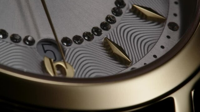 Luxury golden swiss made women watch with diamonds and ribbed pattern rotating while second arrow running by numbers and date. Closeup of flickering gems