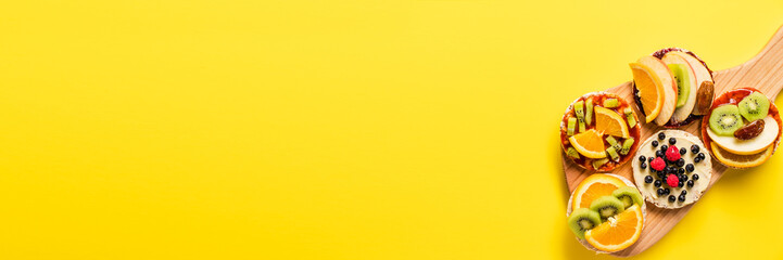 Crispy puffed rice cakes on board with fresh fruit kiwi banana apple blueberries raspberries and orange on the yellow background - top view on healthy organic vegetarian or vegan breakfast gluten free