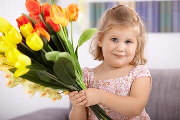 Cute little girl holding bouquet of tulips, smiling, looking at camera.