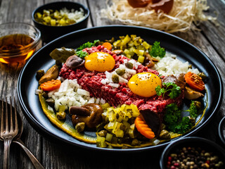 Perfect beef tartare steak with onion, capers, pickled cucumbers and mushrooms on wooden table
