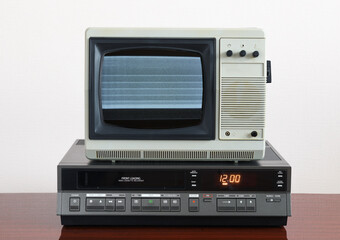 Old silver vintage TV with noise and interference on the screen and VCR on the background of the wallpaper.