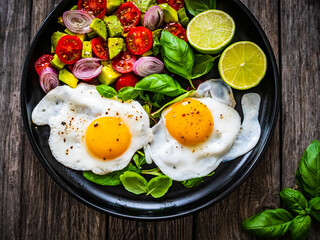 Sunny side up eggs with avocado, cherry tomatoes, toasted bread and red onion on wooden table

