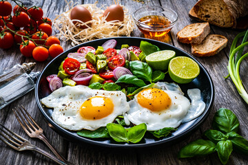 Sunny side up eggs with avocado, cherry tomatoes, toasted bread and red onion on wooden table

