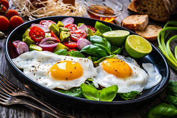 Sunny side up eggs with avocado, cherry tomatoes, toasted bread and red onion on wooden table

