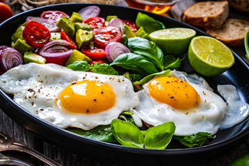 Sunny side up eggs with avocado, cherry tomatoes, toasted bread and red onion on wooden table

