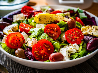 Fresh Greek salad - feta cheese, cherry tomatoes, artichokes, lettuce, black olives and onion on wooden table
