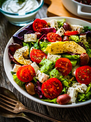 Fresh Greek salad - feta cheese, cherry tomatoes, artichokes, lettuce, black olives and onion on wooden table
