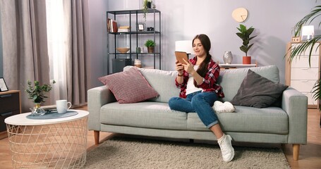 Obraz premium Woman shopping online while chilling at home on sofa. Girl using tablet while typing credit card details. Cropped shot of a woman using her card to make an online payment