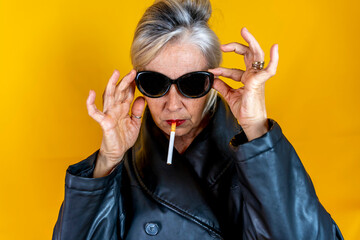 Funny portrait of mature woman. Sophisticated lady having fun dressed in a leather coat smoking a...