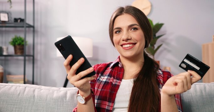 Beautiful caucasian woman sitting on sofa ine room and using smartphone while making shopping online payment. Modern woman private time at home and internet shopping