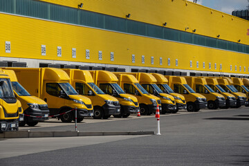 A lot of yellow delivery vans are parking in front of a warehouse, waiting to be loaded.