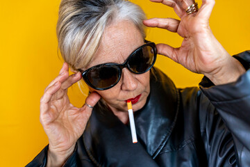 Funny portrait of mature woman. Sophisticated lady having fun dressed in a leather coat smoking a...
