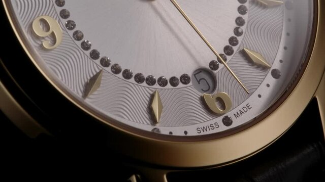 Second arrow running by numbers and date on luxury golden swiss made women watch with diamonds and ribbed pattern. Closeup with zoom-in effect