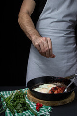 Scrambled eggs on a dark background. Fried eggs with fried sausages. Tasty breakfast. Unhealthy food. Hand salt food
