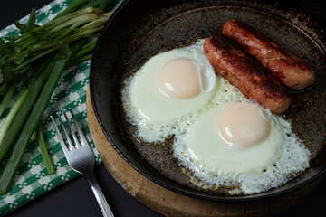 Scrambled eggs on a dark background. Fried eggs with fried sausages. Tasty breakfast. Unhealthy...