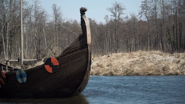 Drakkar floats on the river. Ancient Viking ship. A harsh journey in a historic ship along the river stream. Ancient sailors. Conquest campaigns. A warship with shields on board.